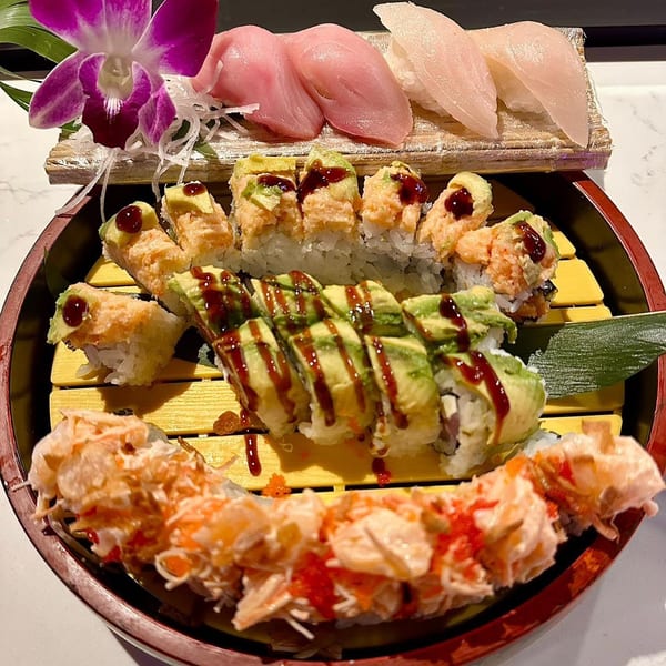 A large platter of various sushi rolls and sashimi, garnished with a purple orchid.