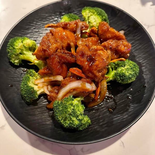 Sweet and sour chicken with broccoli and onions on a black plate.