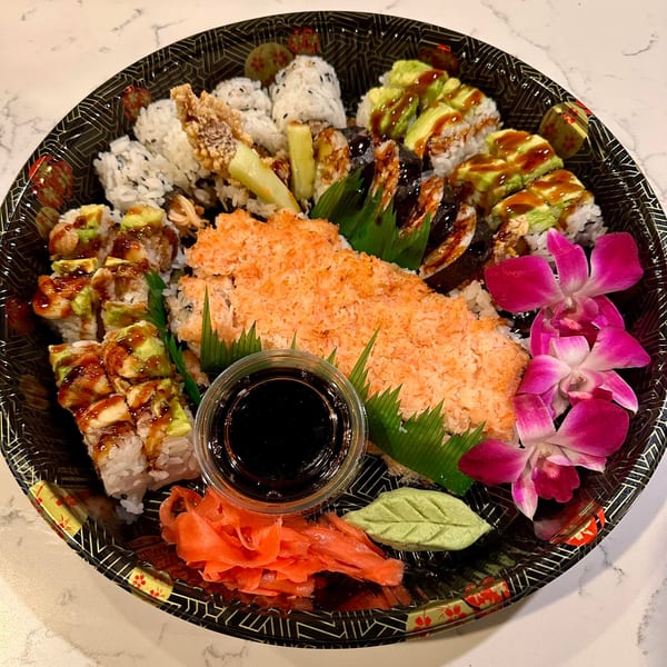 A large sushi platter with various rolls, ginger, wasabi, soy sauce, and pink orchids.