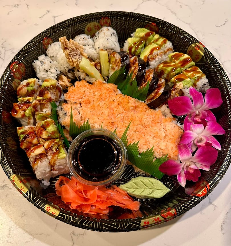 A large sushi platter with various rolls, ginger, wasabi, soy sauce, and pink orchids.