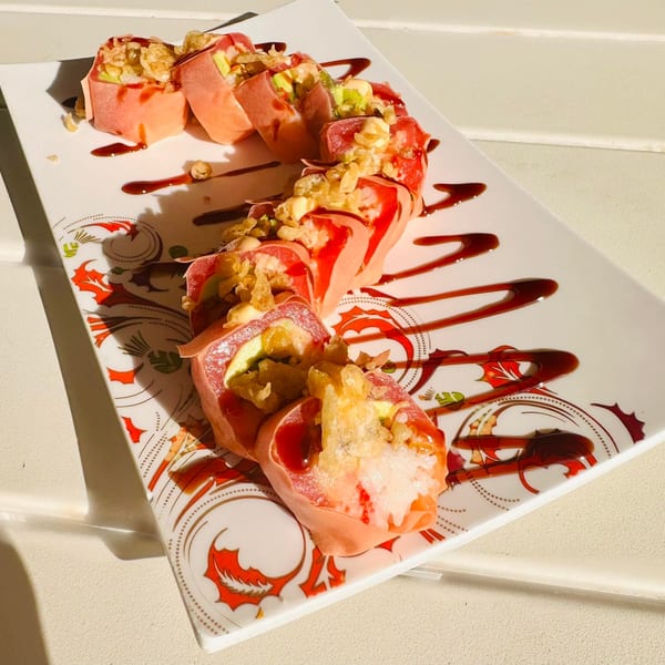Pink sushi rolls with avocado, topped with crispy fried onions and drizzled with dark sauce.