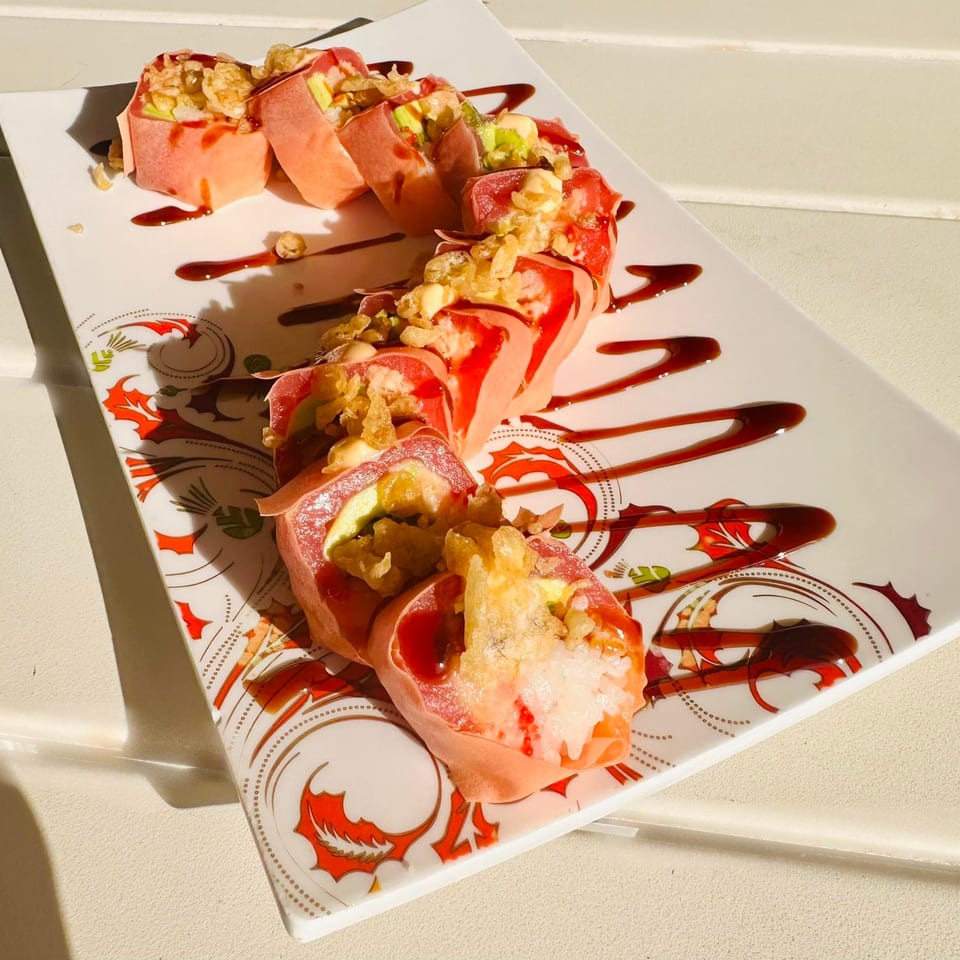 Pink sushi rolls with avocado, topped with crispy fried onions and drizzled with dark sauce.