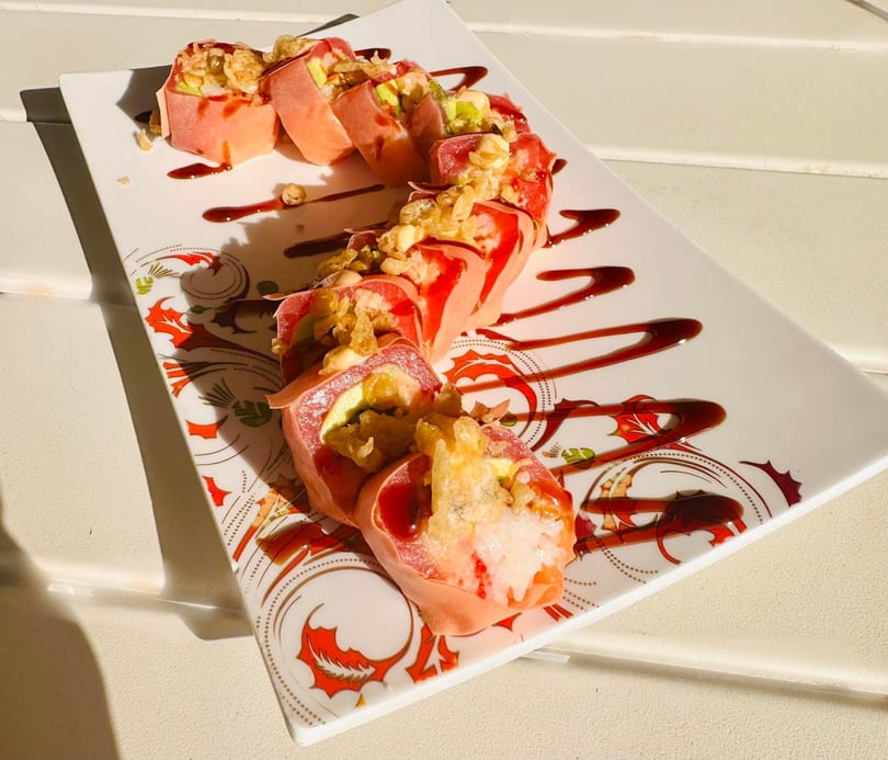 Pink sushi rolls with avocado, topped with crispy fried onions and drizzled with dark sauce.